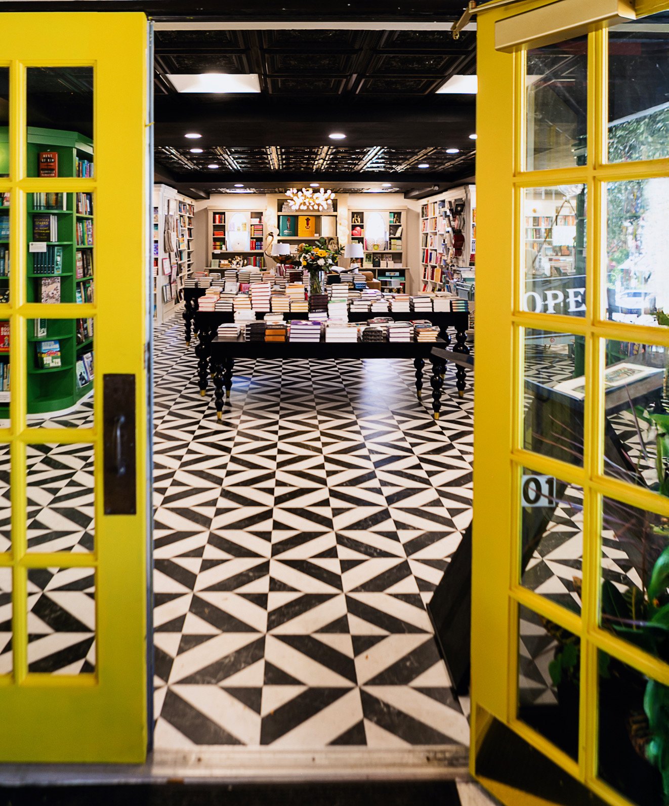 Open yellow doors into Books on Third, with black-and-white tile and book tables inside.