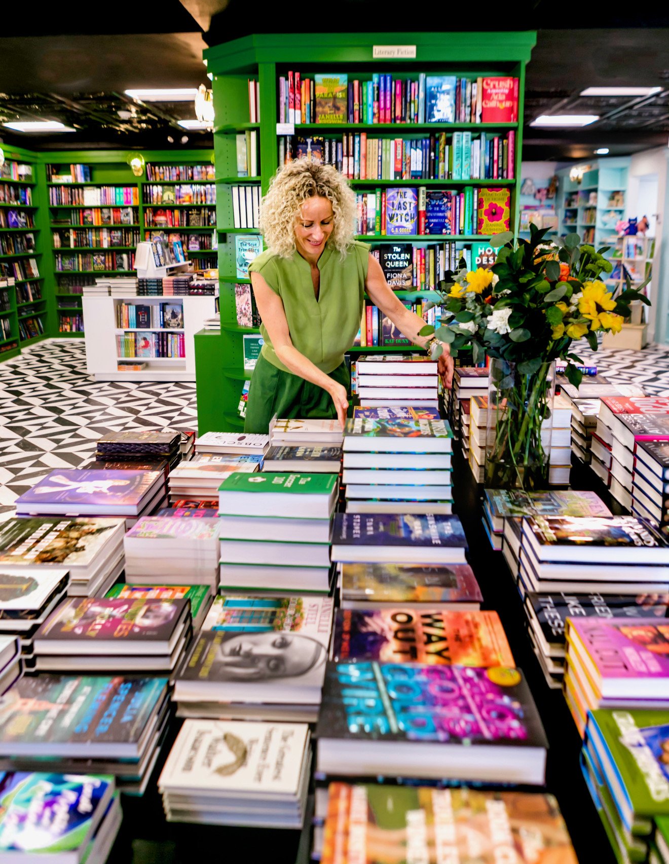 Inside Books on Third: green Literary Fiction shelves and stacked books on a display table.